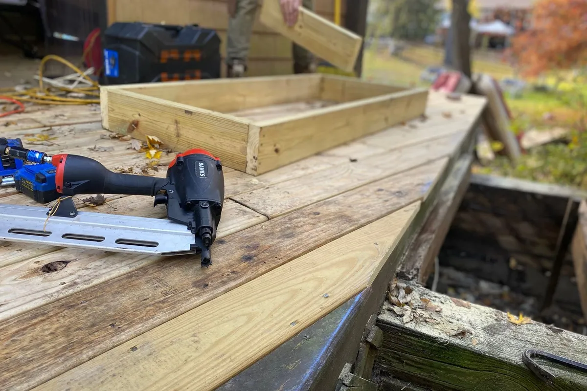 Close-up of a nail gun and wooden frame during deck construction, highlighting carpentry work.